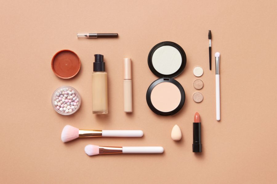 Makeup sample with makeup products and brushes on orange background